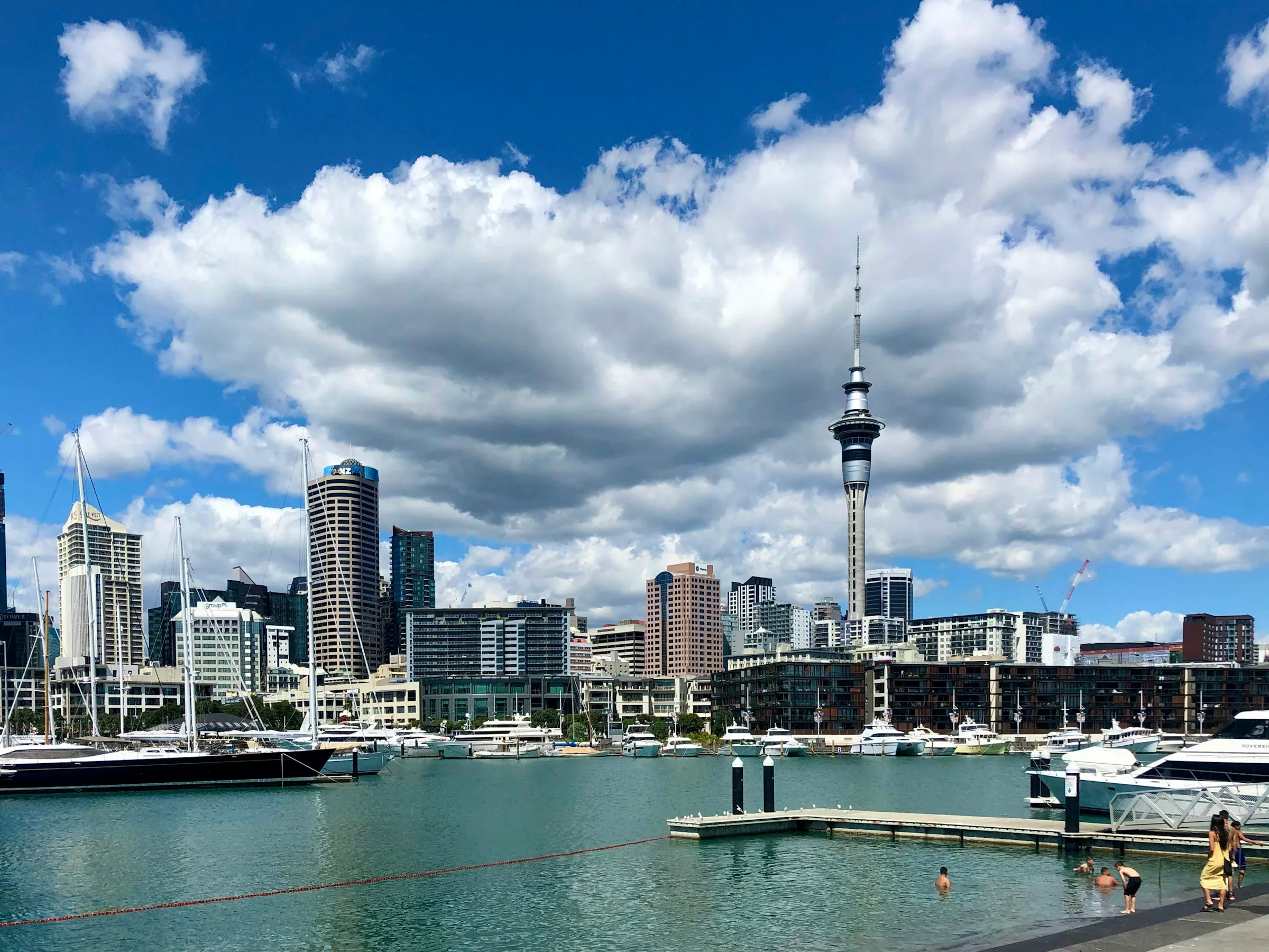 Auckland's CBD towers and the Sky Tower under a blue sky with white clouds