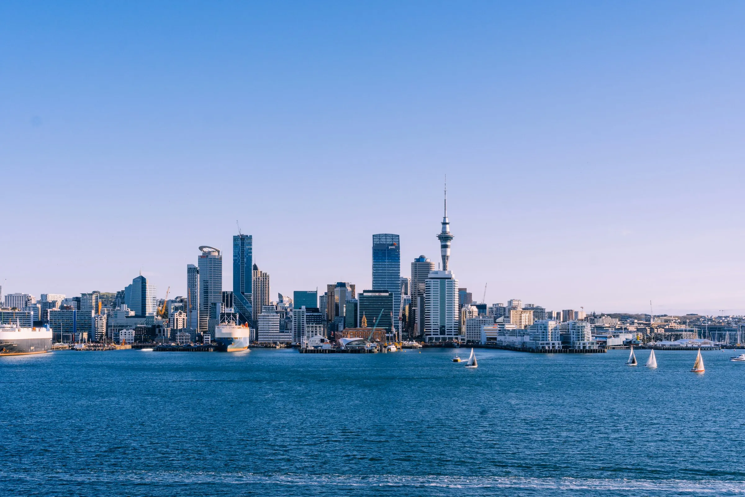 Auckland's skyline and Sky Tower across the Waitematā Harbour under a blue sky