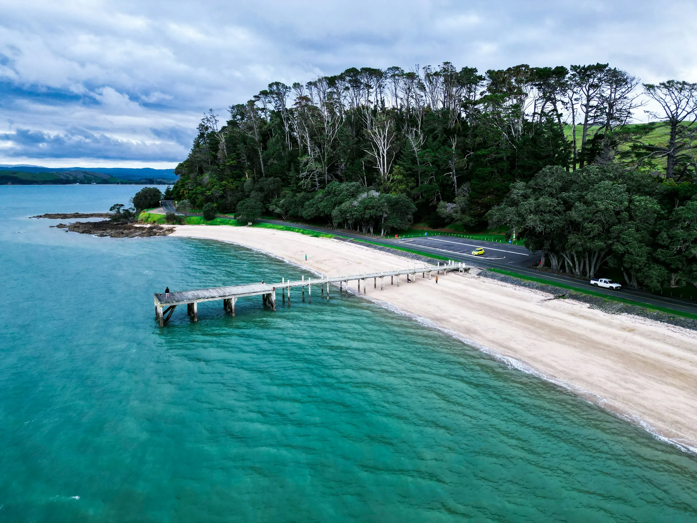 A white-sand beach and jetty beside turquoise water near Auckland