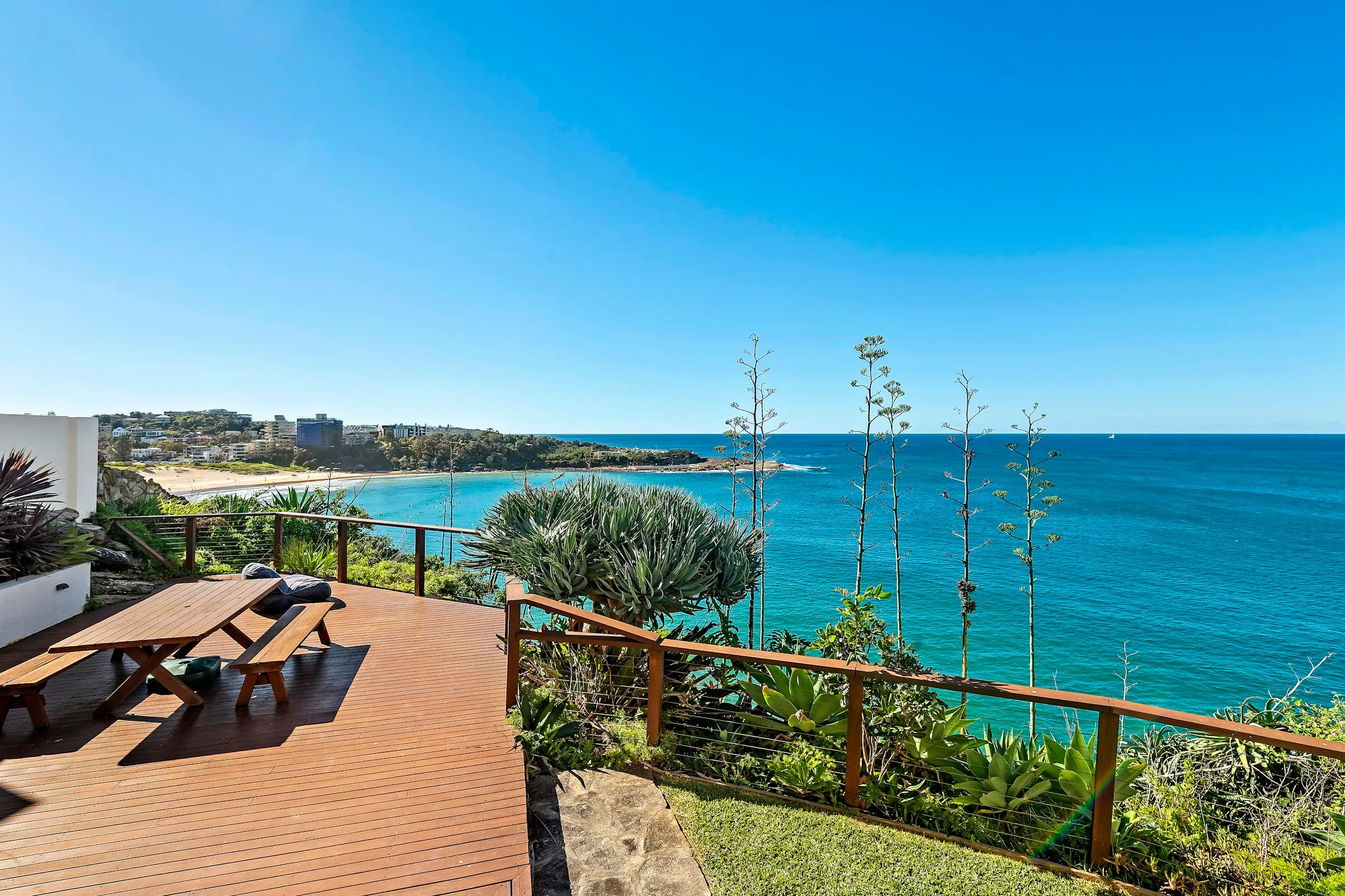 A timber deck with a picnic table overlooking a sandy bay and blue ocean on a clear day